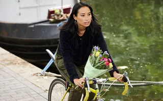 Woman cycles past moored narrowboats on the towpath