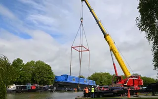 Wide shot of a crane lifting a blue narrowbiat into water