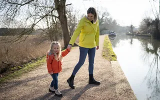 A mother and daughter hold hands as they walk along the towpath.