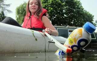 Girl picks litter out of the water from a kayak