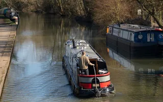 Narrowboat moves along the canal in dappled sunlight.