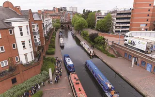 An aerial shot of a narrowboat passing other moored boats and surrounded by high-rise flats.