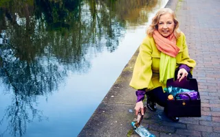 A woman kneels on the towpath to pick up a plastic bottle