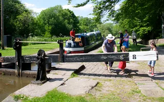 Family push lock gates shut behind a narrowboat in the sun