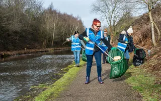 Group of women in winter hats and high vis using litter pickers and bags along a towpath