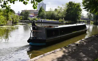 A narrowboat passes along the canal on a sunny day with the city in the background