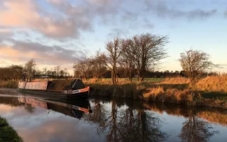 A narrowboat moored at sunset, reflected in the canal