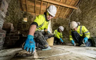 Workers in high vis and hard hats laying flagstones in old stone building