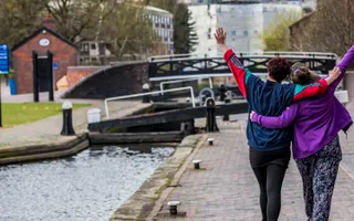 Two adults with their arms around each other as they walk along a canal lock in Birmingham.