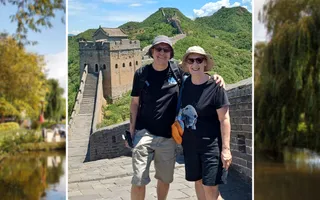 A man and woman stand together smiling with the Great Wall of China in the background.