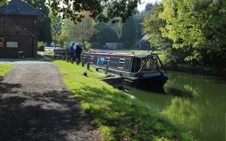 Boat moored up on the canal on a sunny day surrounded by green trees
