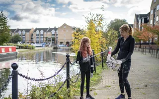 Mother and daughter collect litter from paved towpath with houses in background