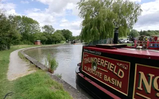 A red boat with the name 'Thunderfield' moors on the towpath.