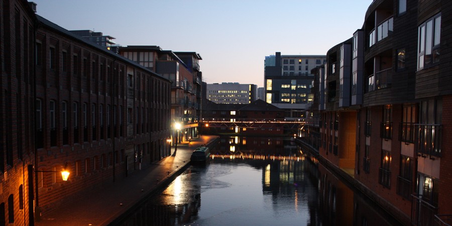 Nightime view of canal between buildings towards illuminated bridge