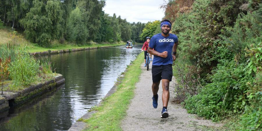 A man running alongside a tree-lined canal in Birmingham