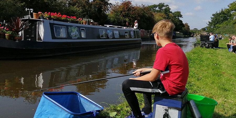 A boat passes Charlie taking part in the 2020 junior canal fishing championships