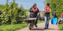 Two young ladies pushing a wheelbarrow along a towpath