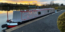 A brand new narrowboat, grey in colour with solar panels on top, on the canal at sunset