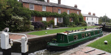 A green canal boat in the locks in front of a brick-built house