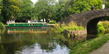 A green narrowboat manoeuvring in the basin with onlookers standing on the bridge