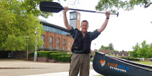 Man standing holding canoe paddle aloft