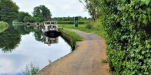 Picture of a towpath along a canal with boats, bushes and grass