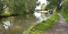 Picture of a well used towpath along a canal with a boat, bushes, grass and trees