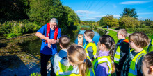 A Canal & River Trust worker stood next to the canal, explaining water safety to a group of school children