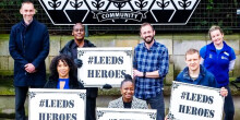 A group of people stand with placards saying #LEEDS HEROES